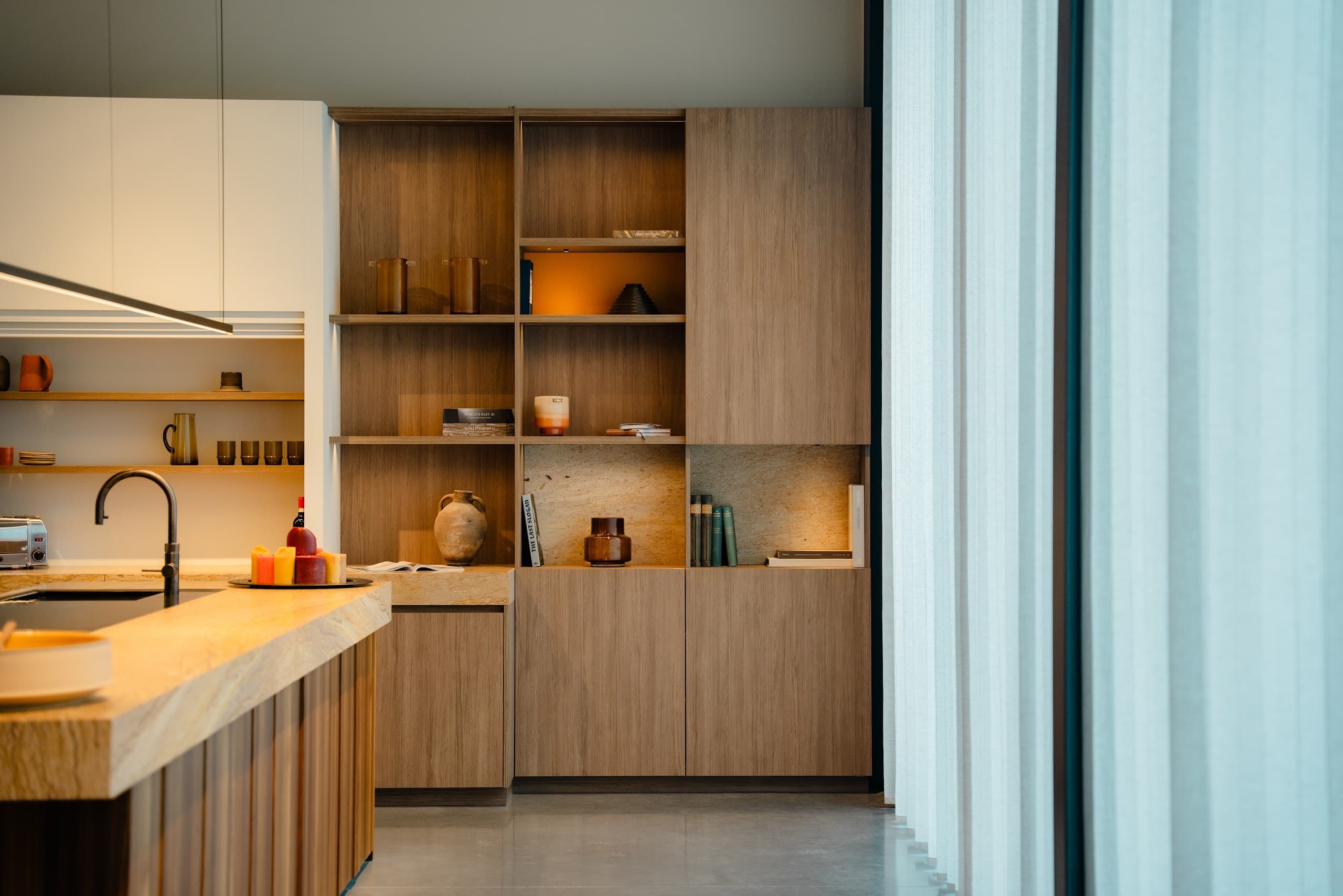 Showroomkeuken met houten wandkast en luchtige gordijnen die het daglicht filteren