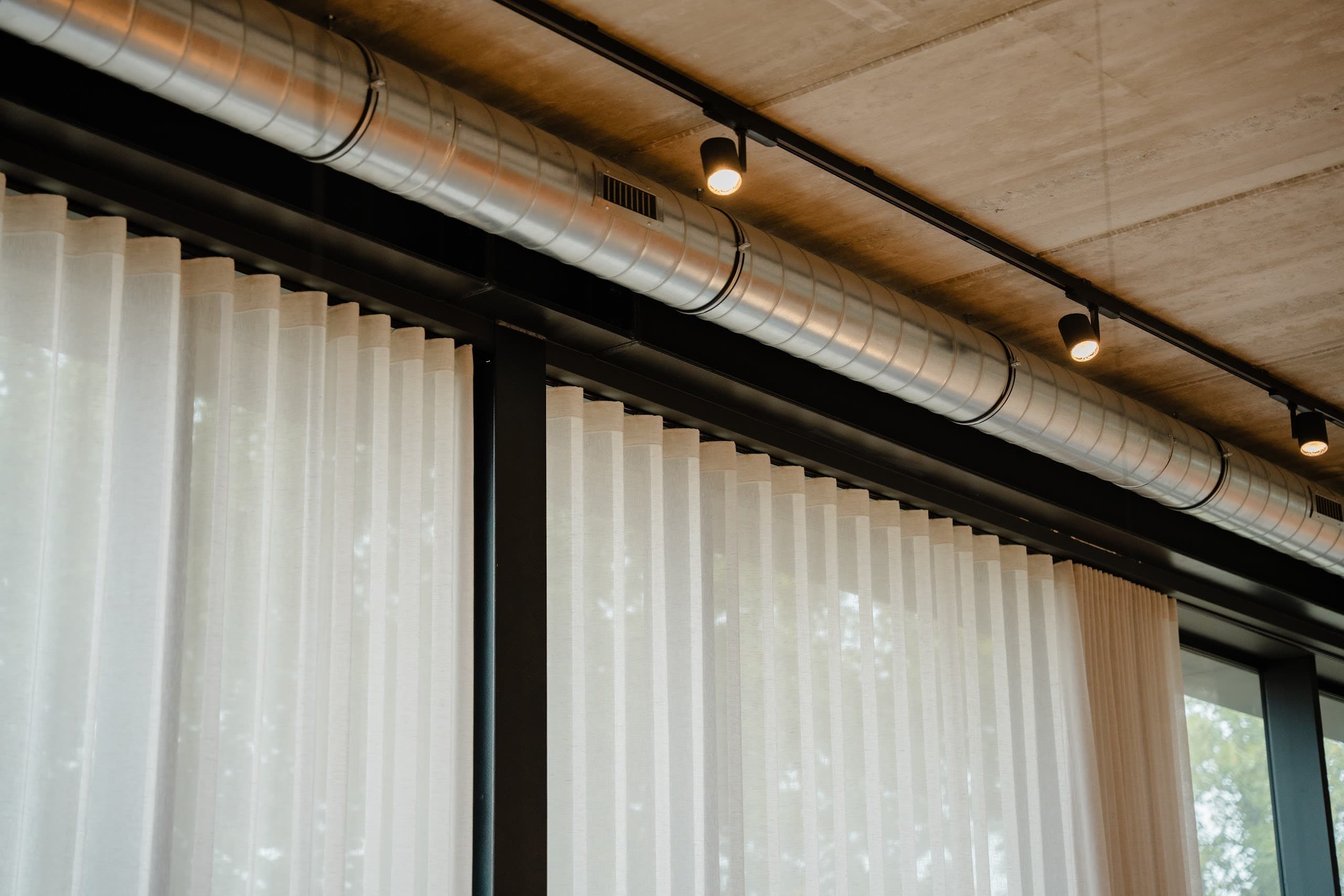 Showroom met betonnen plafond en transparante gordijnen langs de volledige glasgevel